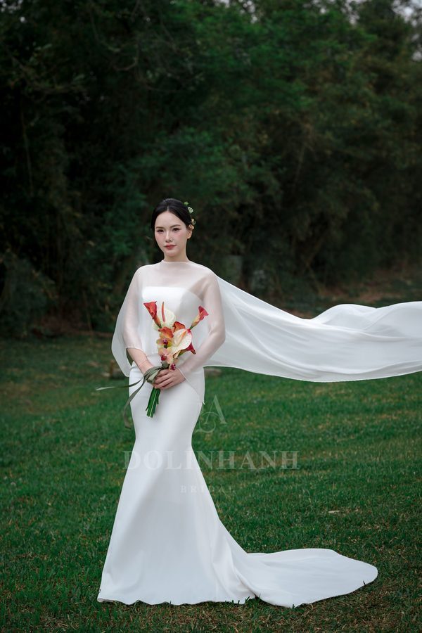 A bride in a sheer chiffon bridal cape walking with the groom on a lawn