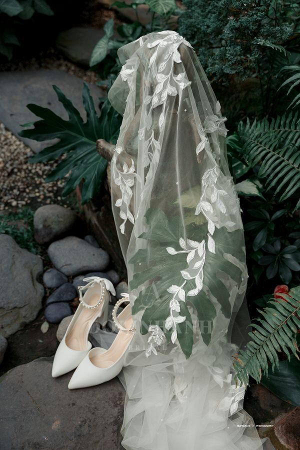 The Cuc Phuong climbing leaf lace cathedral wedding veil on a bride by a brick wall