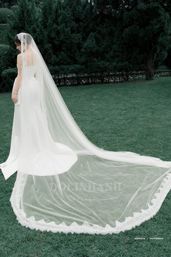 The Da Lat lace edge cathedral wedding veil spread across a garden lawn