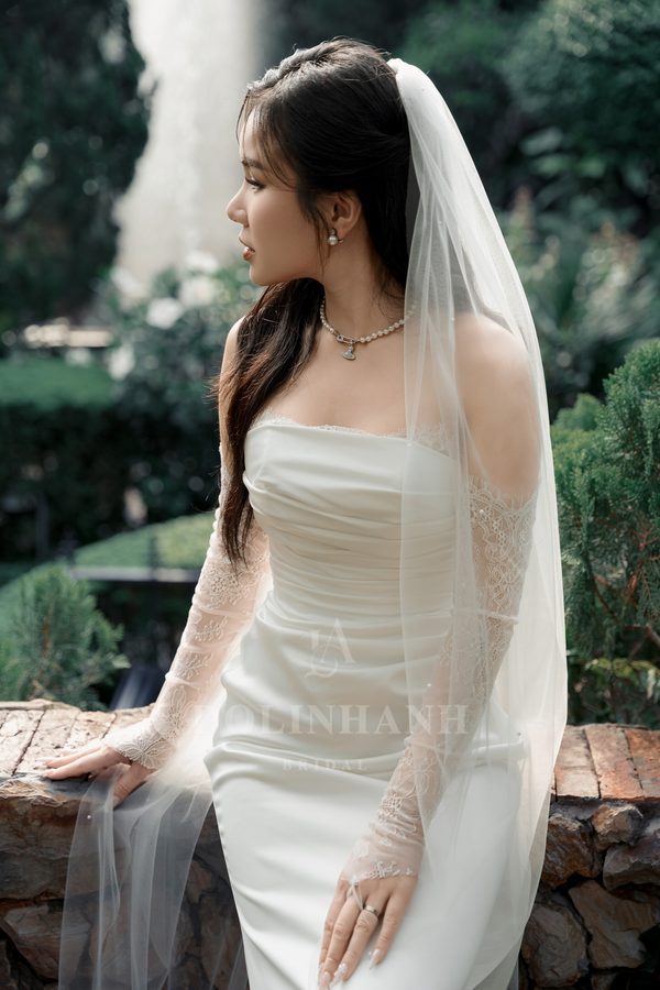 Sheer lace bridal gloves on a bride resting her hand on a garden wall