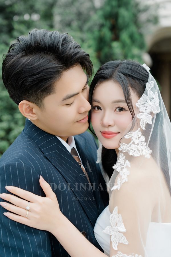 The Pu Luong lace flower veil framing a bride's face beside the groom