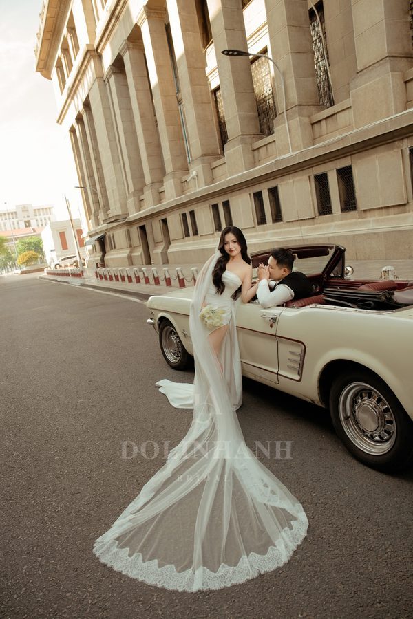 The Sai Gon geometric lace mantilla cathedral veil on a bride by a classic car