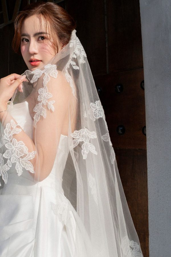 The Tam Dao lace appliqué wedding veil framing a bride's face